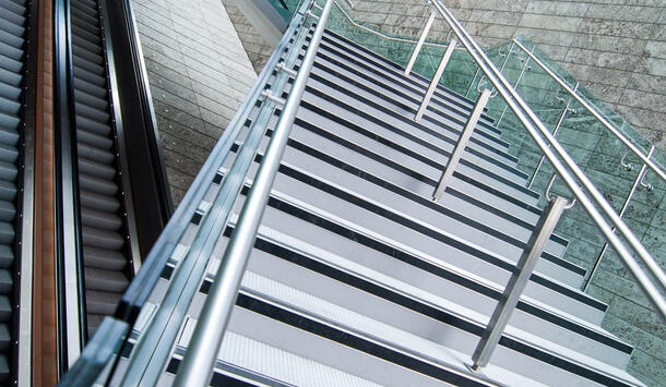 Das Foto zeigt zwei Rolltreppen sowie eine Treppe, die über die beiden Rolltreppen führt. Die Rolltreppen laufen gerade aus.  Die moderne aus Metall bestehende Treppe überquert die Rolltreppen, jedoch versetzt im Zickzack. 