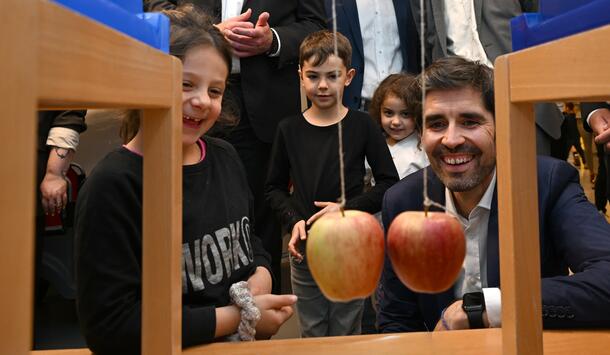 Sven Teuber, Bildungsminister Rheinland-Pfalz betrachtet mit zwei Schülerinnen und einem Schüler ein MINT-Experiment mit zwei Äpfeln